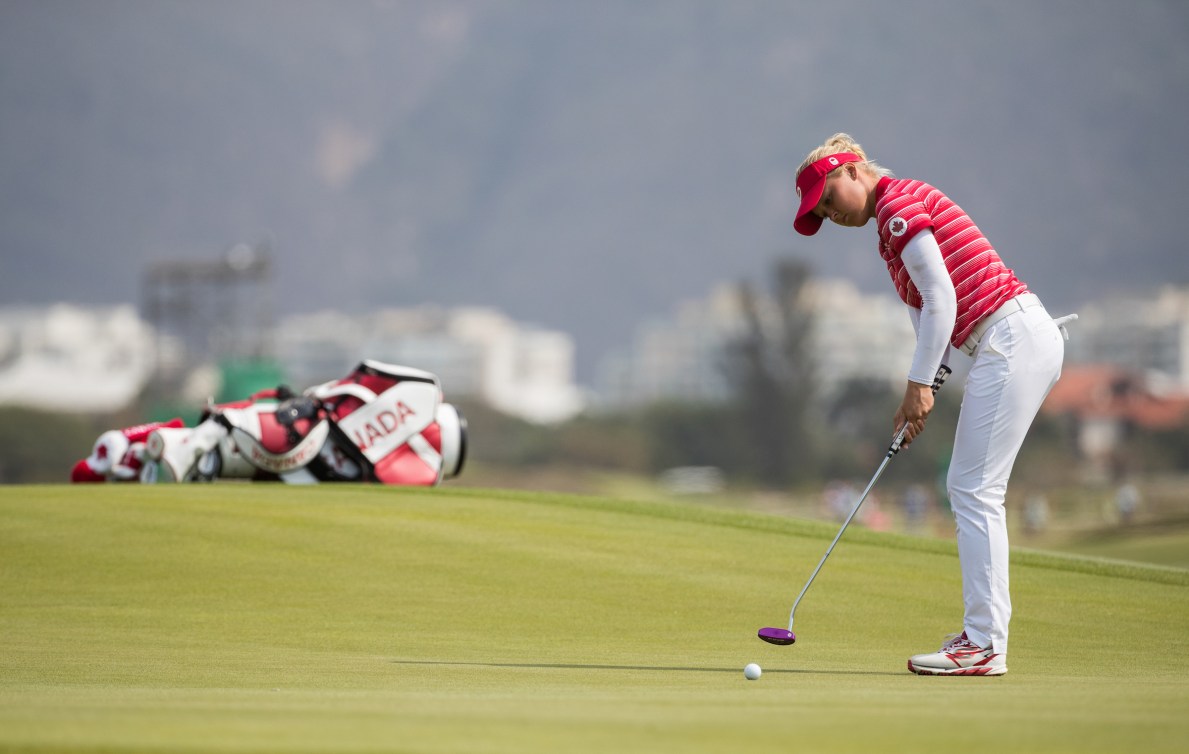 Wide shot of Brooke Henderson putting with her golf bag lying on its side in the background 