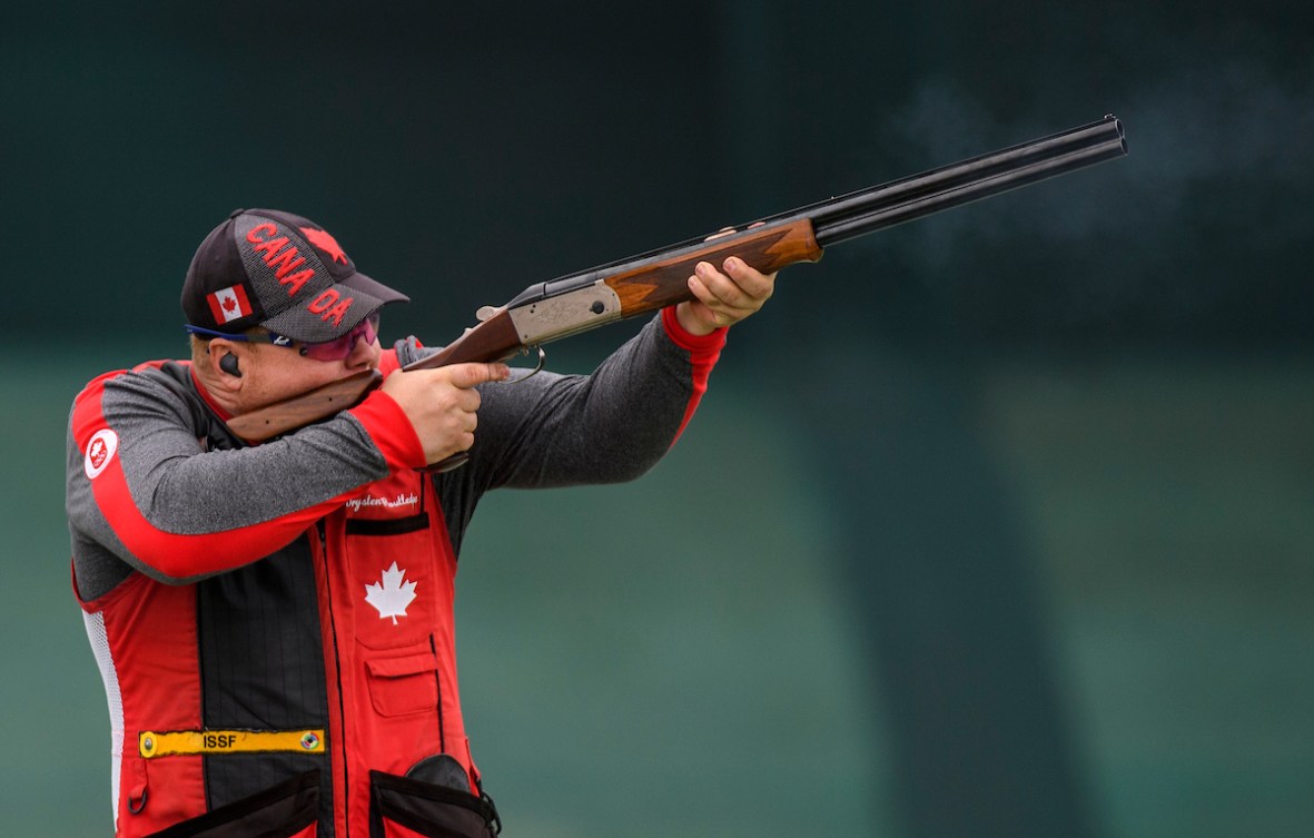 A male shooting athlete fires a shotgun