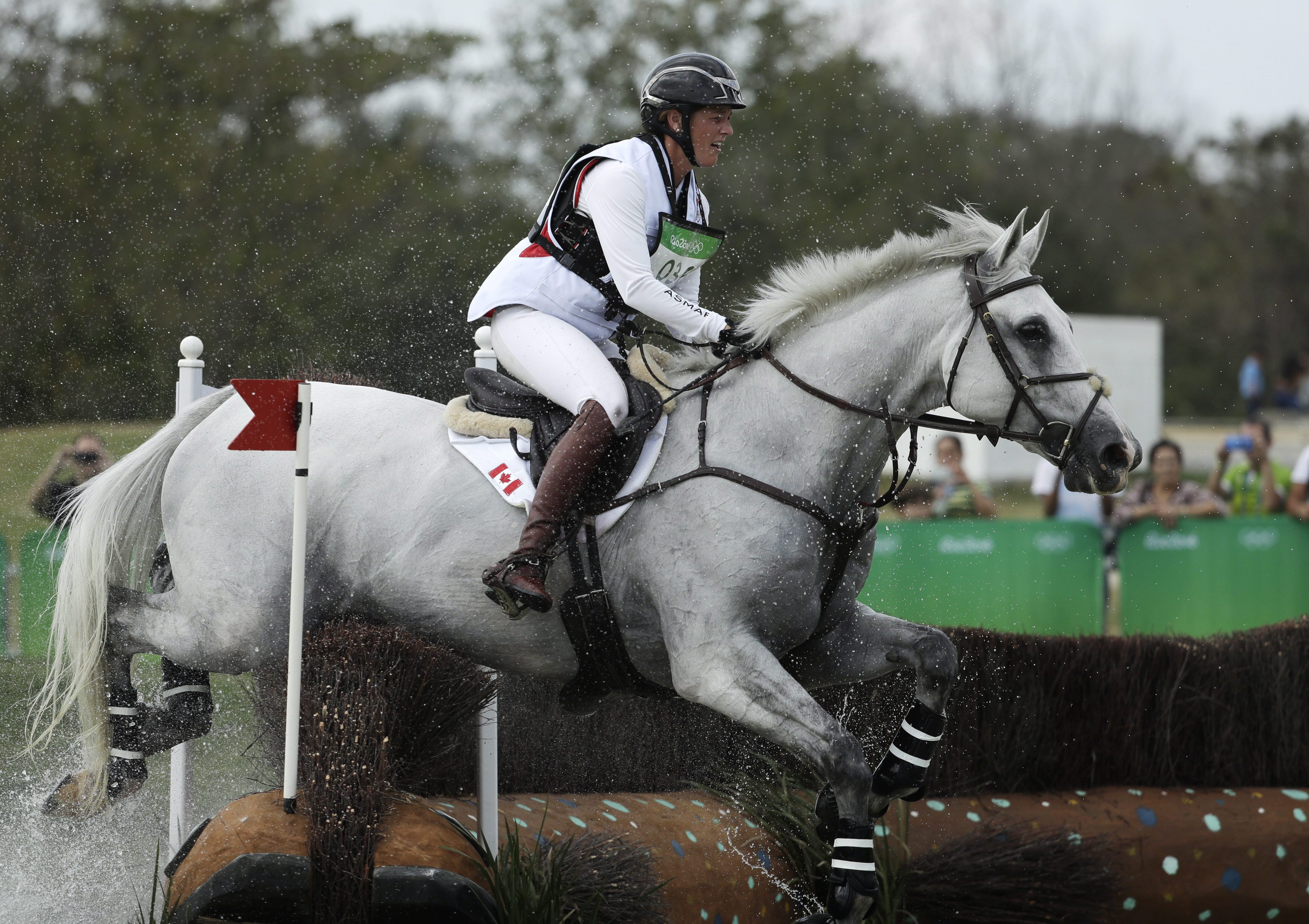 Colleen Loach rides a white horse over a water obstacle in a cross country event