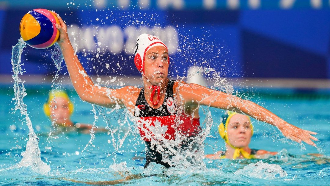 A Canadian female water polo player holds the ball in the ait above the water preparing to throw