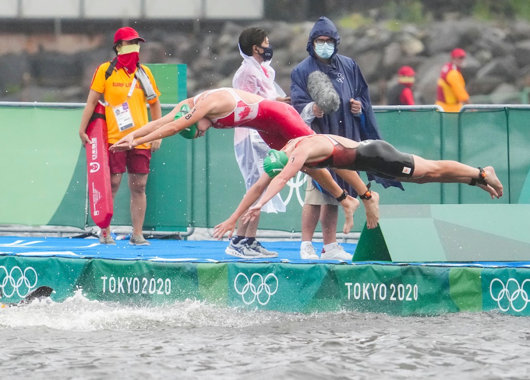 Two triathletes dive from a pontoon into the water 