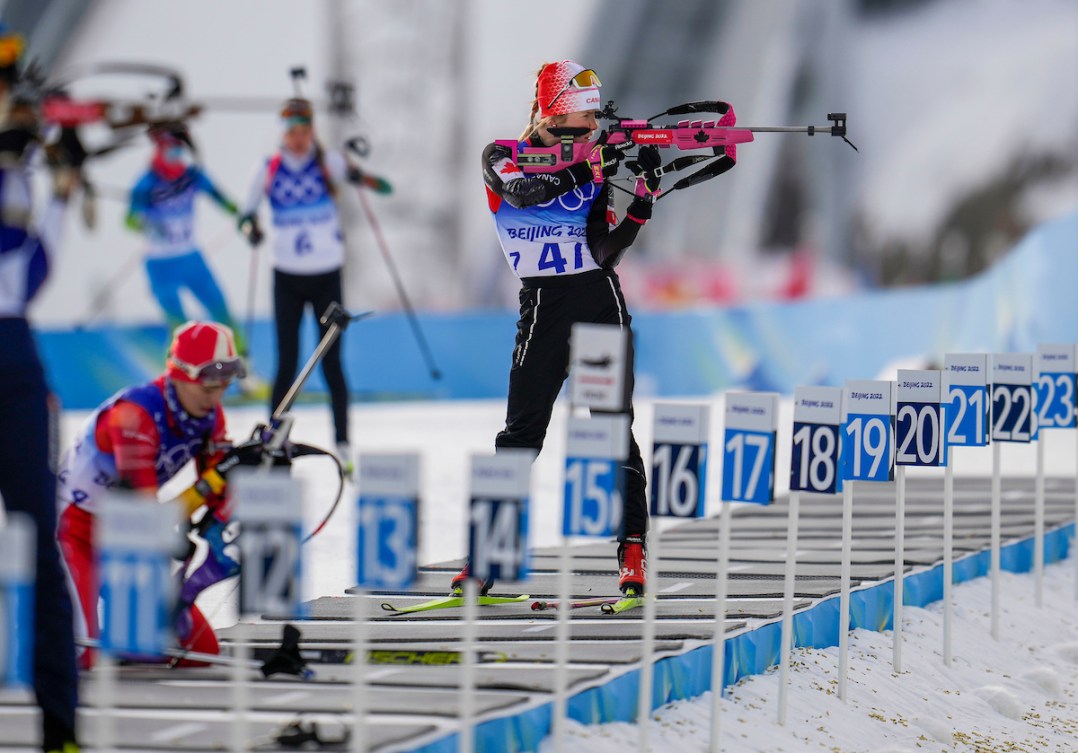 A biathlete stands in the shooting range preparing to fire her rifle 