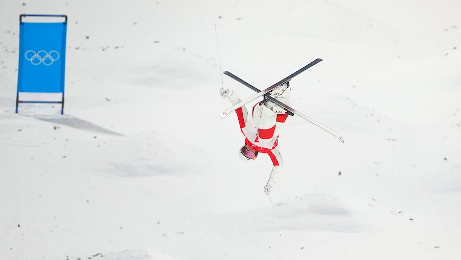 Mikael Kingsbury performs an aerial trick with his skis crossed on a moguls course