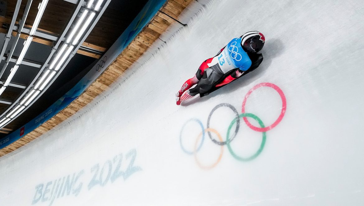 Skeleton racer slides over the Olympic rings on an ice track