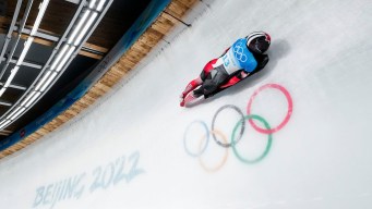 Skeleton racer slides over the Olympic rings on an ice track