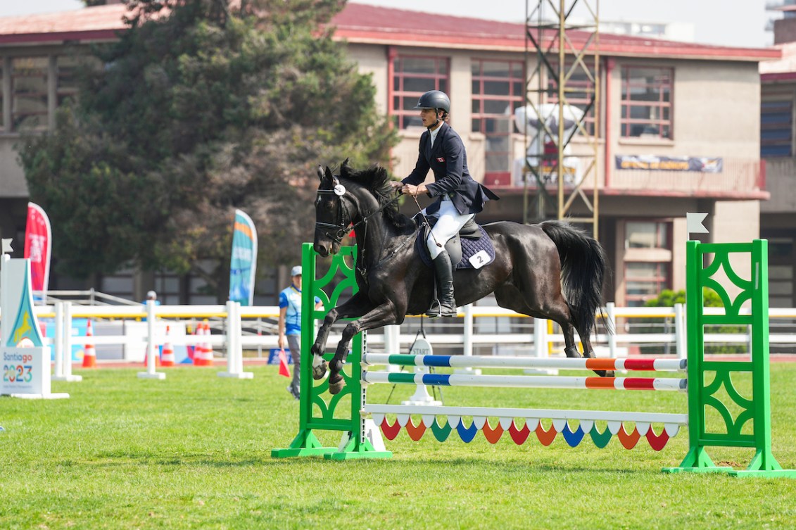 A rider in a dark jacket rides a dark brown horse jumping over an obstacle 