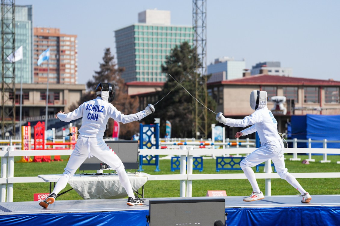 Two fencers tap their swords on an outdoor piste 