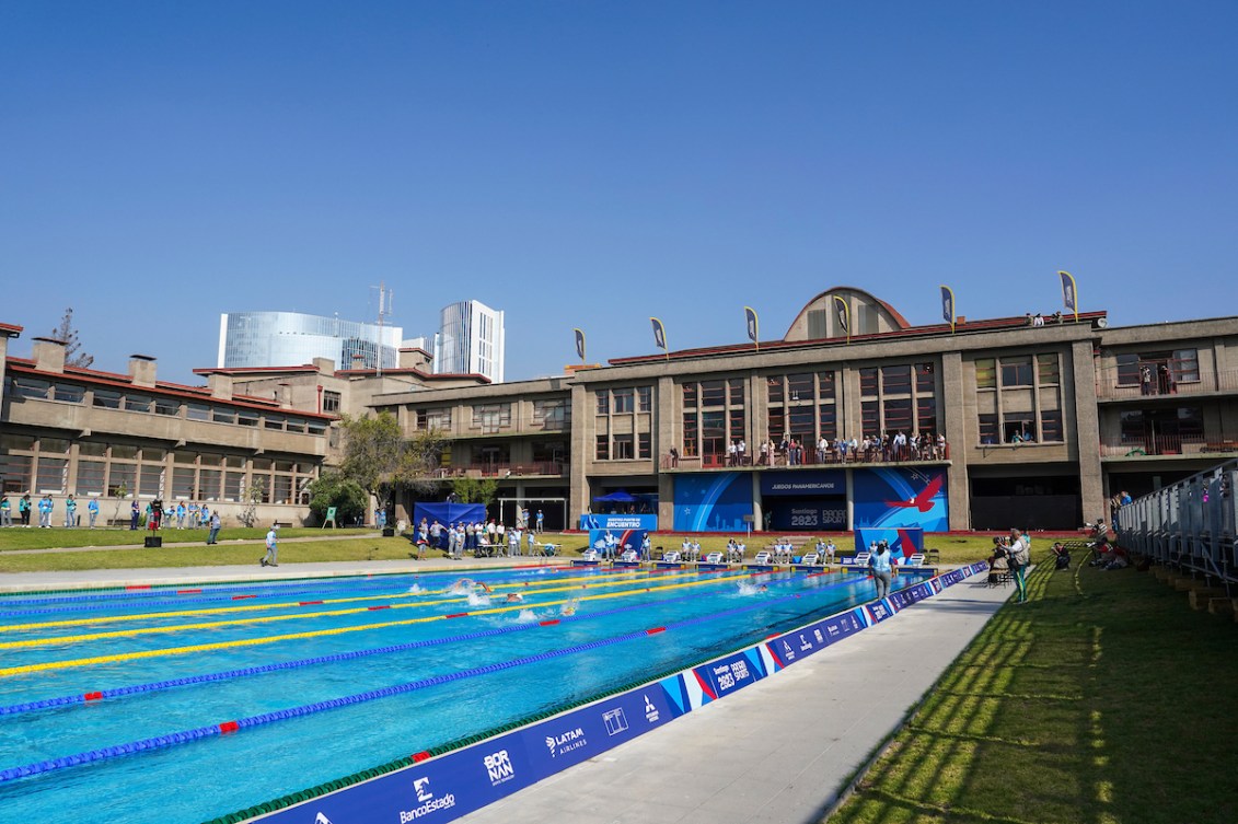 Wide shot of an outdoor swimming pool with swimmers racing in lanes 