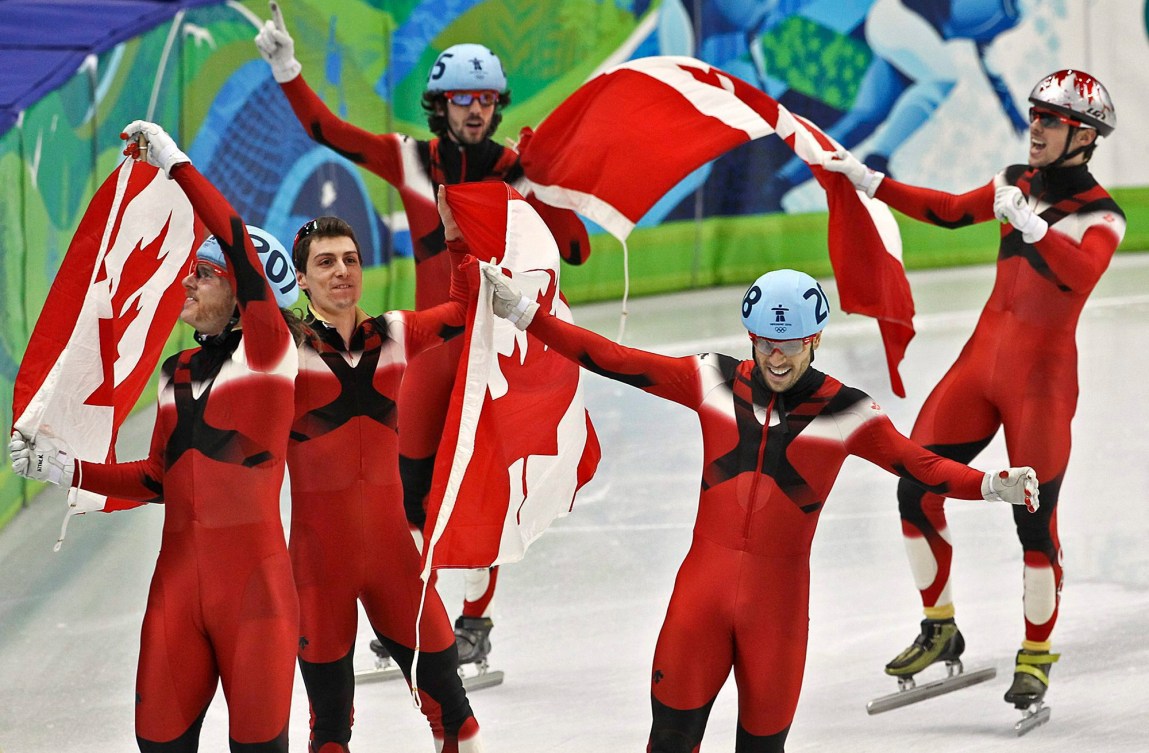 5 short track speed skaters carry Canadian flags in a victory lap 