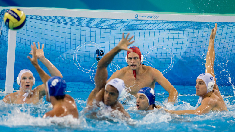 Men's water polo players battle for the ball in front of the net