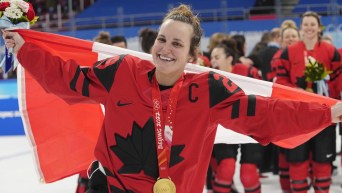 Marie-Philip Poulin smiles with the Canadian flag draped behind her like a cape