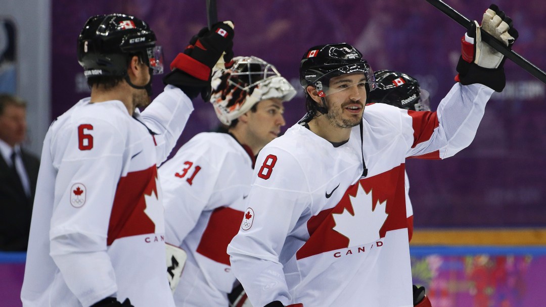 Three Canadian hockey players in white jerseys raise sticks in celebration