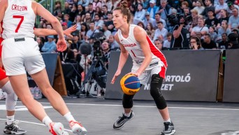 Michelle Plouffe in a white jersey and shorts dribbles a basketball