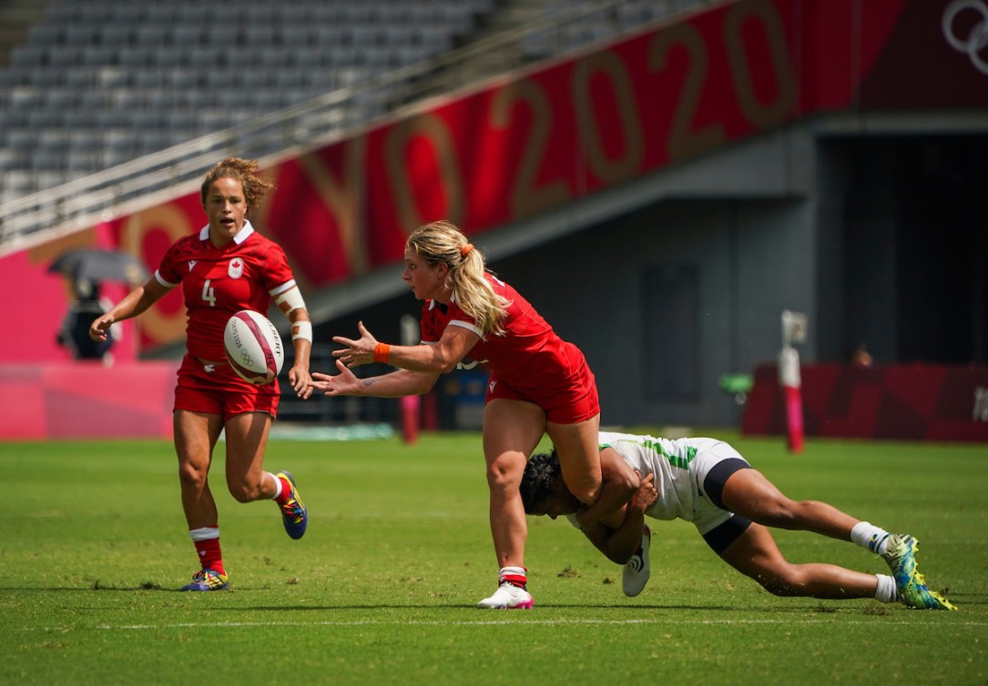 A rugby player passes the ball to her teammate while being tackled