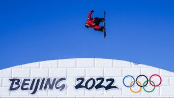 Sebastien Toutant grabs his board as he flips in the air over a Beijing 2022 sign