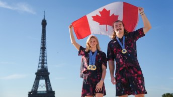 Summer McIntosh and Ethan Katzberg wear Olympic gold medals while holding the Canadian flag in front of the Eiffel Tower