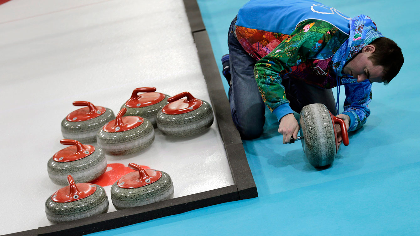 An ice crew worker makes adjustments to curling rocks at Sochi 2014. 