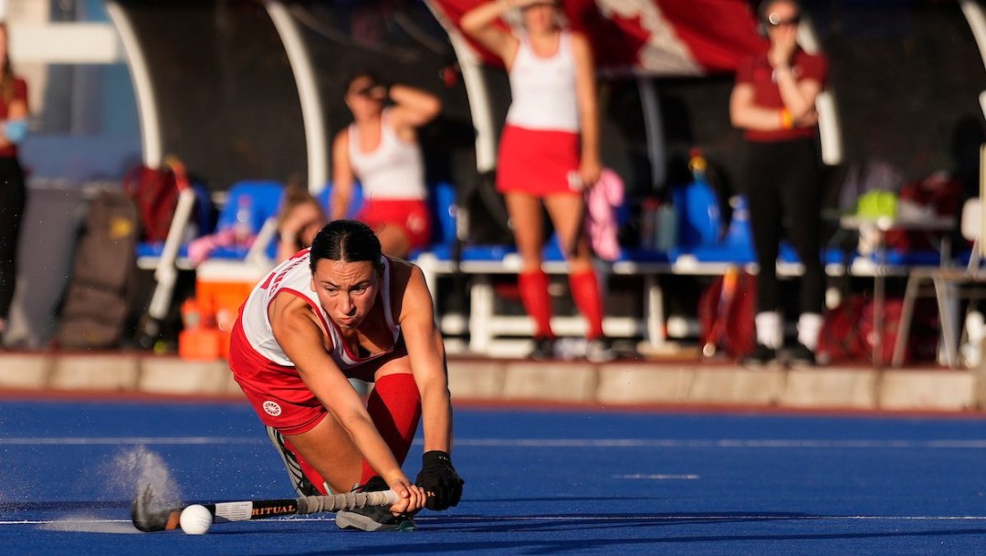A field hockey player gets low to play the ball