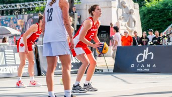 Katherine Plouffe in a red basketball jersey and shorts prepares to throw the ball at the net