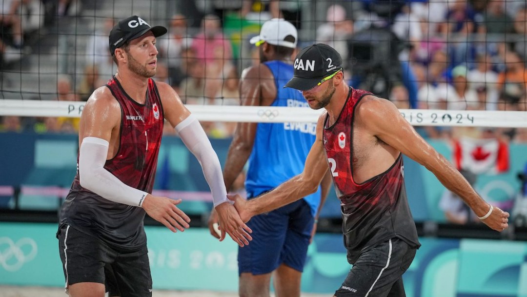 Sam Schachter and Daniel Dearing high five while standing in front of a volleyball net