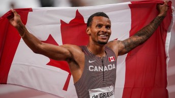 Andre De Grasse holds a Canadian flag up behind his back and head