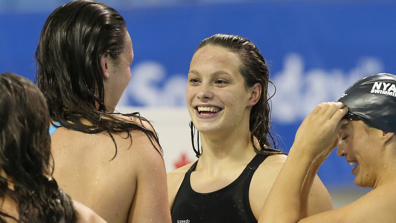Penny Oleksiak (centre) after her Canadian and world junior record-setting swim in the 100m free at Rio Trials on April 9, 2016 (Photo: Scott Grant via Swimming Canada).