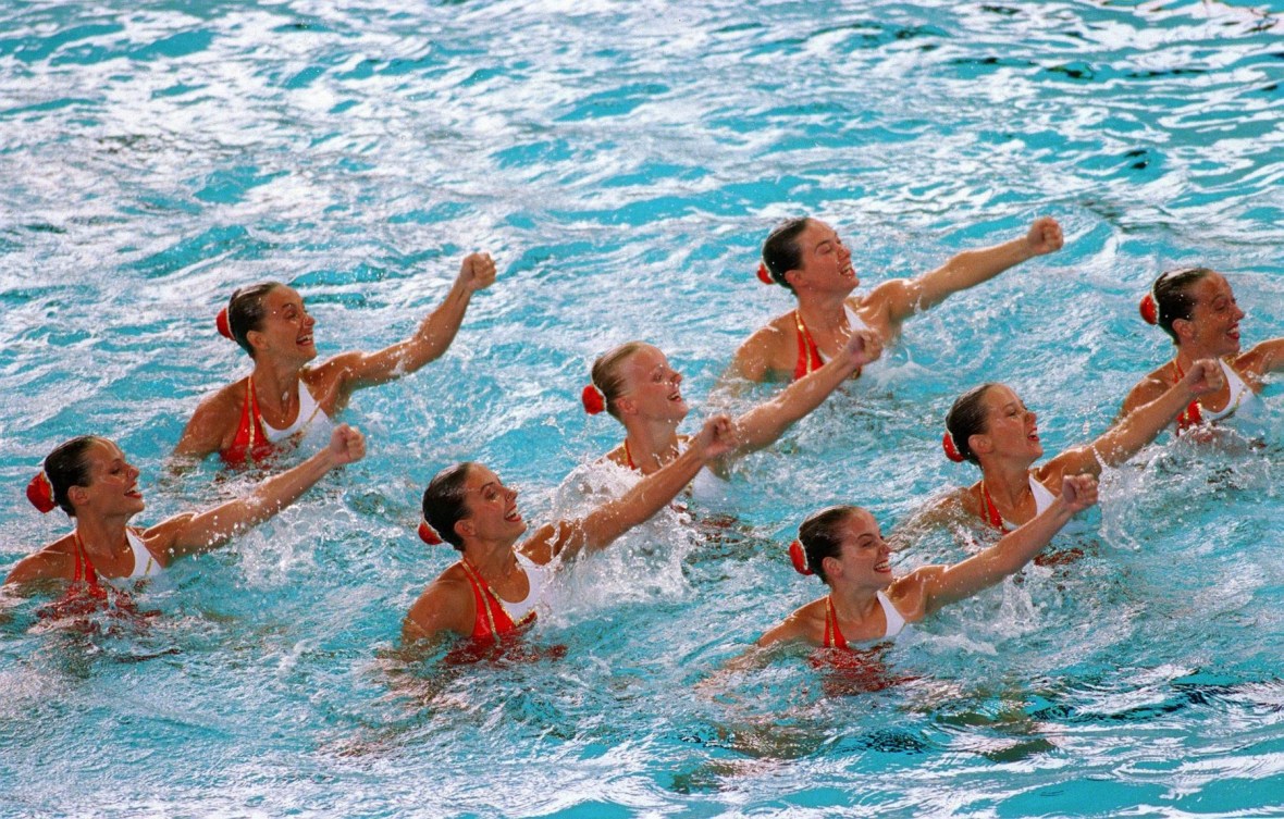 Eight synchronized swimmers in three lines perform arm movements in the water 
