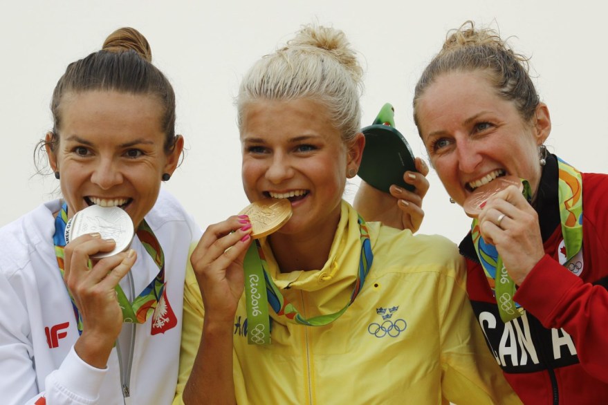 Gold medalist Jenny Rissveds of Sweden, center, silver medalist Maja Wloszczowska of Poland, left, and bronze medalist Catharine Pendrel of Canada, right, bite they medals on the podium of the women's cross-country mountain bike race at the 2016 Summer Olympics in Rio de Janeiro, Brazil, Saturday, Aug. 20, 2016. (AP Photo/Patrick Semansky)