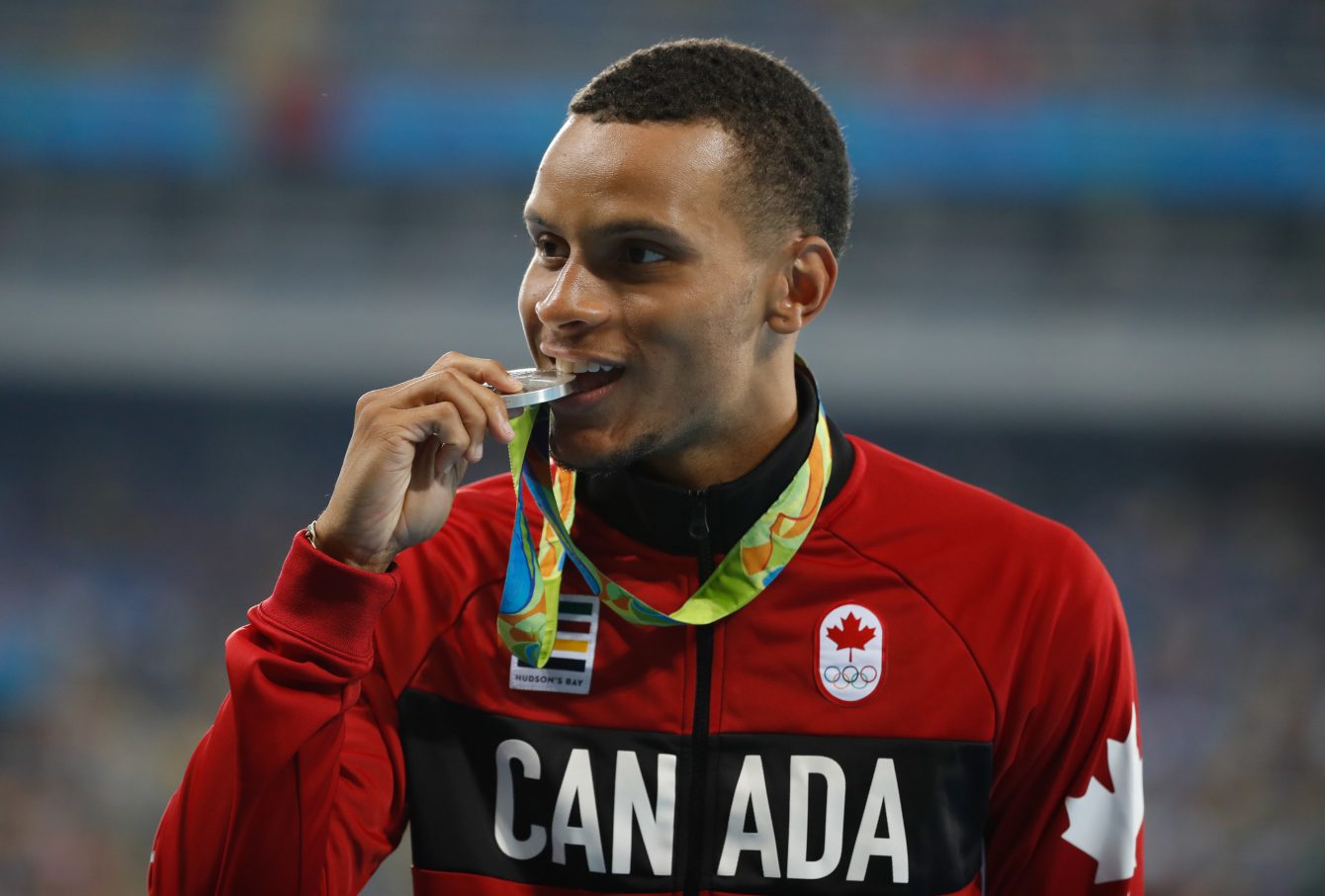 Andre De Grasse bites his 200m silver medal at Rio 2016. (August 19, 2016. COC Photo/Mark Blinch)