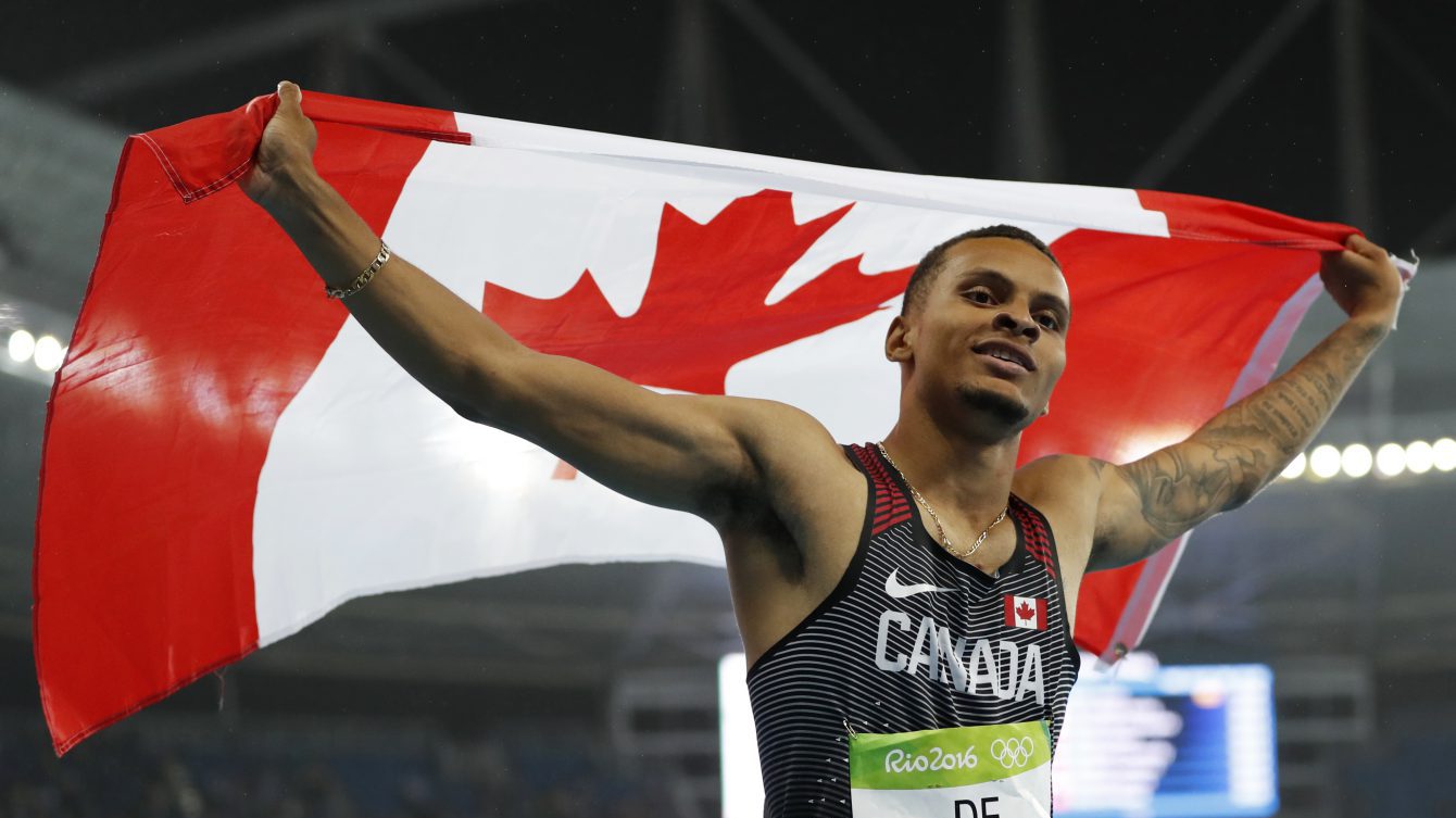 Canada's Andre De Grasse celebrates with his nation's flag after earning a silver medal in the men's 200m final in Rio on August 18, 2016. (photo/ Stephen Hosier)