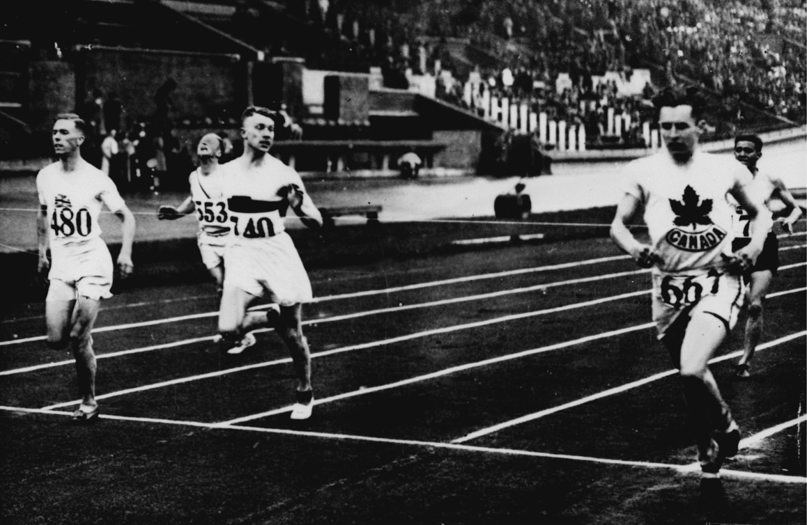 Black and white photo of men running across the finish line of a sprint race 