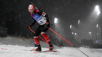 Christian Gow skis at night in snowfall during a biathlon race