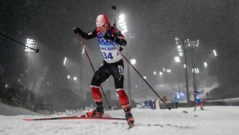 Scott Gow skis at night in snowfall during a biathlon race