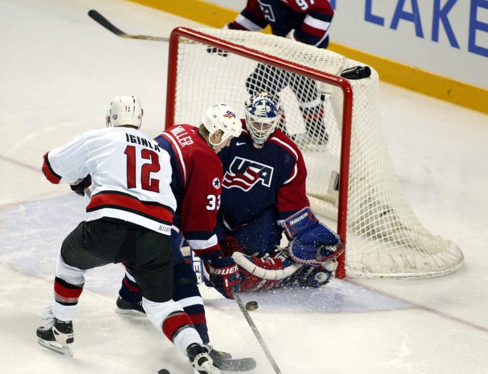 Jarome Iginla in a white jersey in front of the American net with the goaltender wearing blue