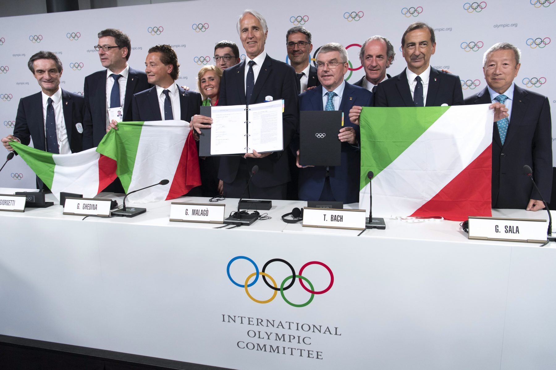 group of people in suits holding italian flags at IOC press conference