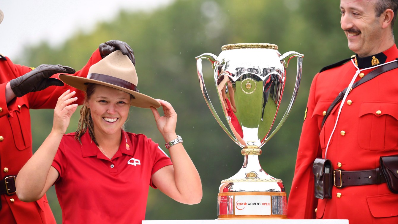 ブルック・ヘンダーソン（Brooke Henderson）がトロフィーの隣に立って、騎馬帽子をかぶっています。