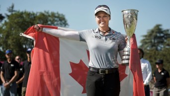 Brooke Henderson holds a trophy and the Canadian flag behind her back