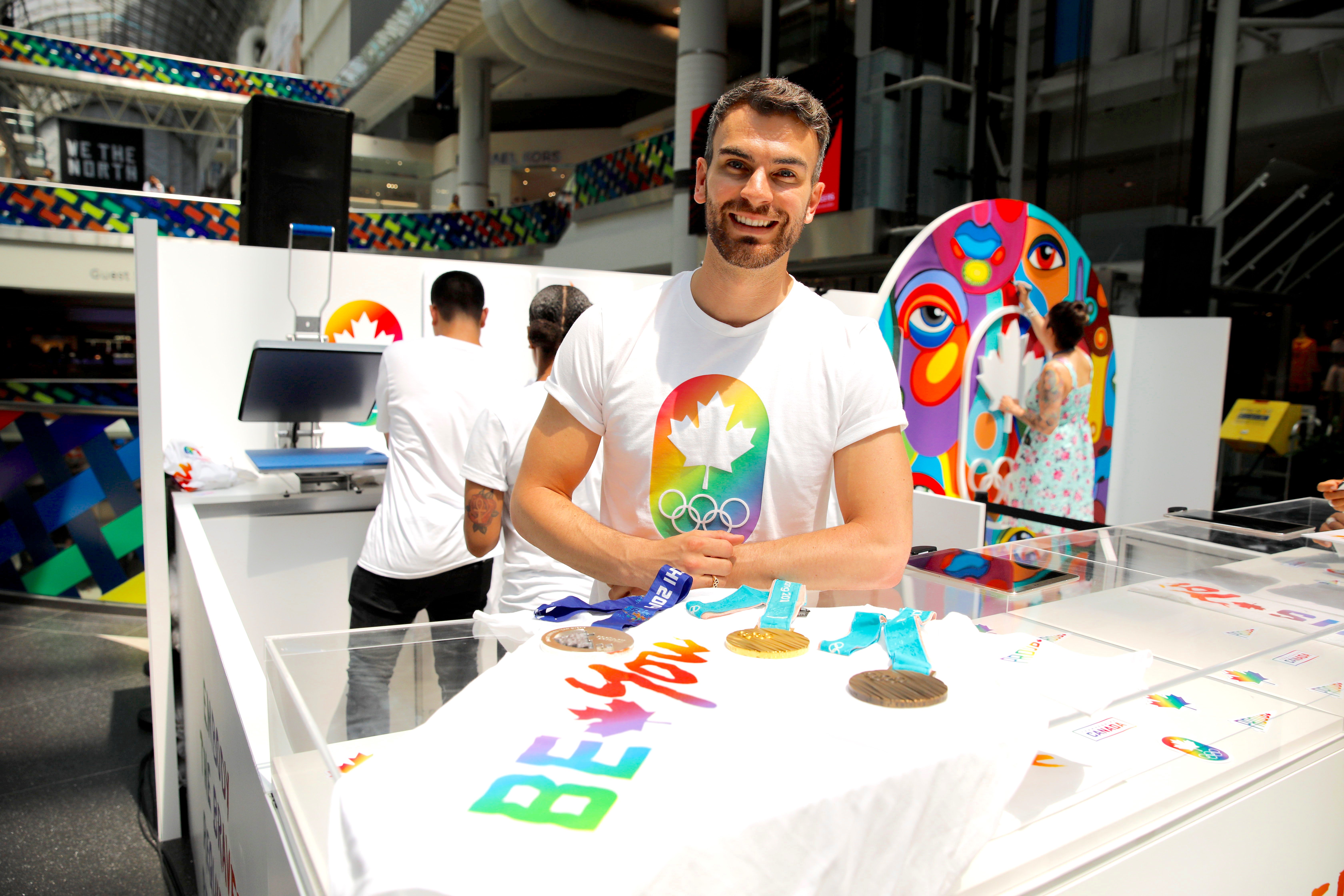 Eric Radford poses in front of the 2019 Be You pop-up with his three Olympic medals.