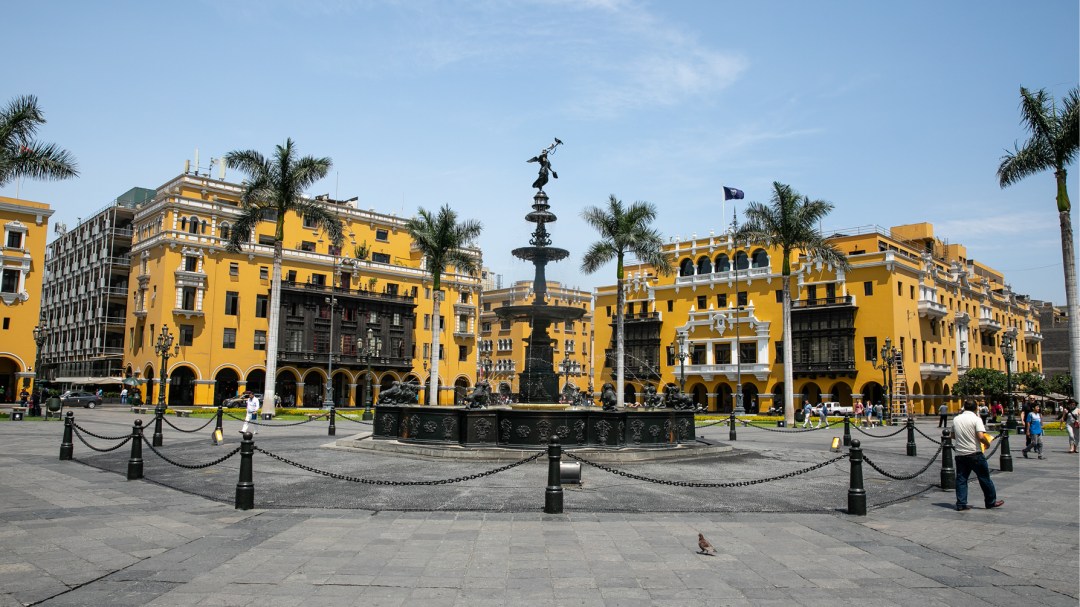 Yellow buildings behind a statue and palm trees in Lima