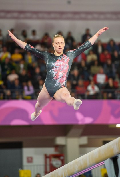 Gymnast does a split leap on the beam
