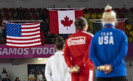 three athletes stand on the podium with the american and canadian flags in the distance