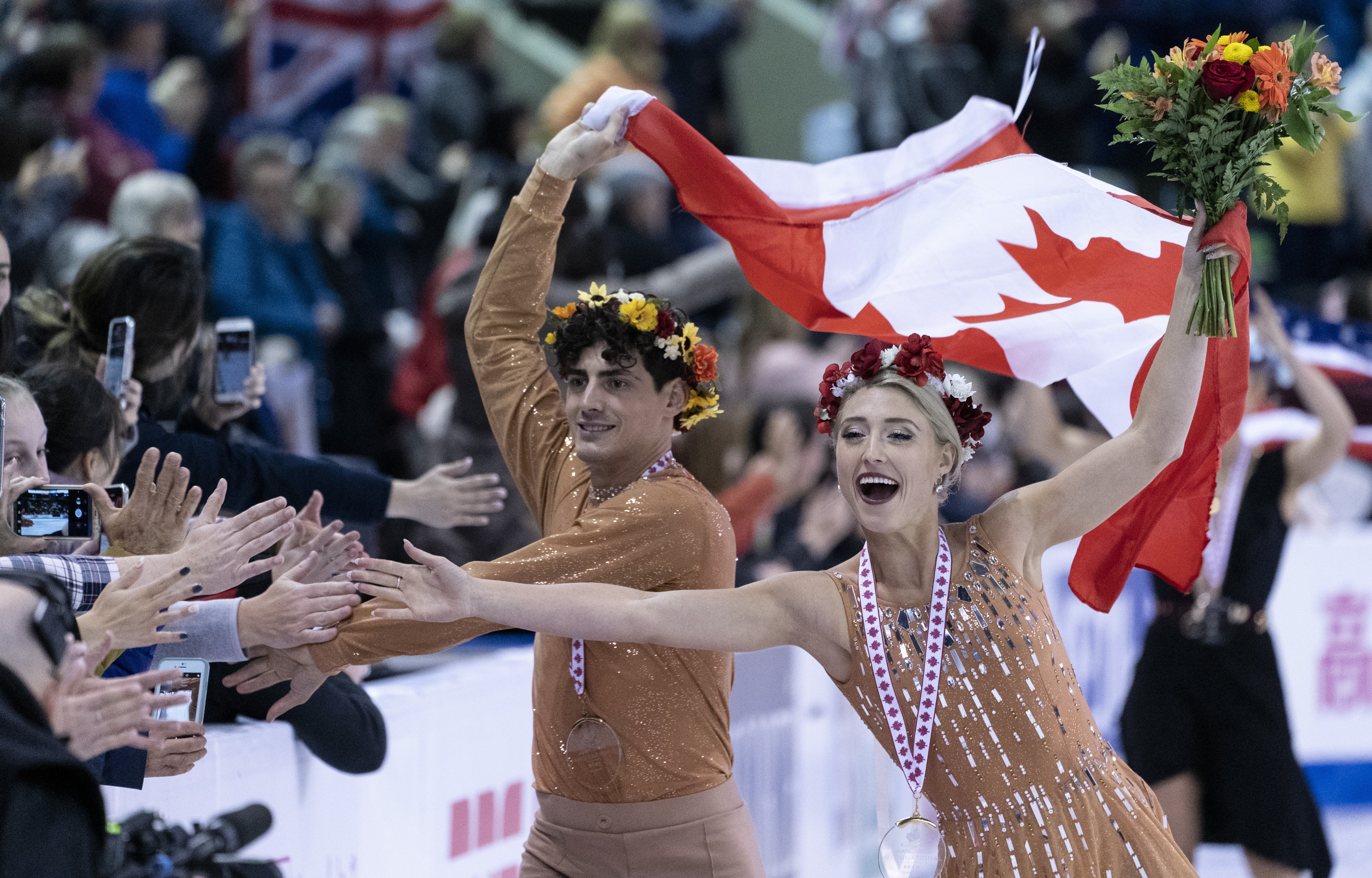 Piper Gilles and Paul Poirier reach out to the crowd during victory ceremonies at Skate Canada