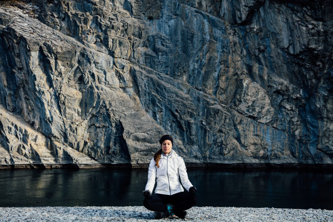 Stephanie Labbé sits cross-legged with her eyes closed in front of a lake and mountains.