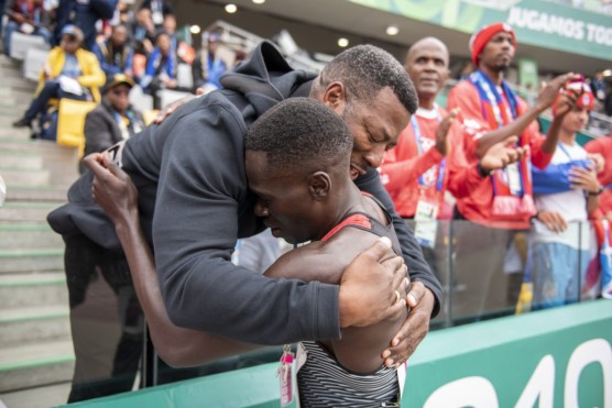 Marco Arop hugs his coach in the stands.