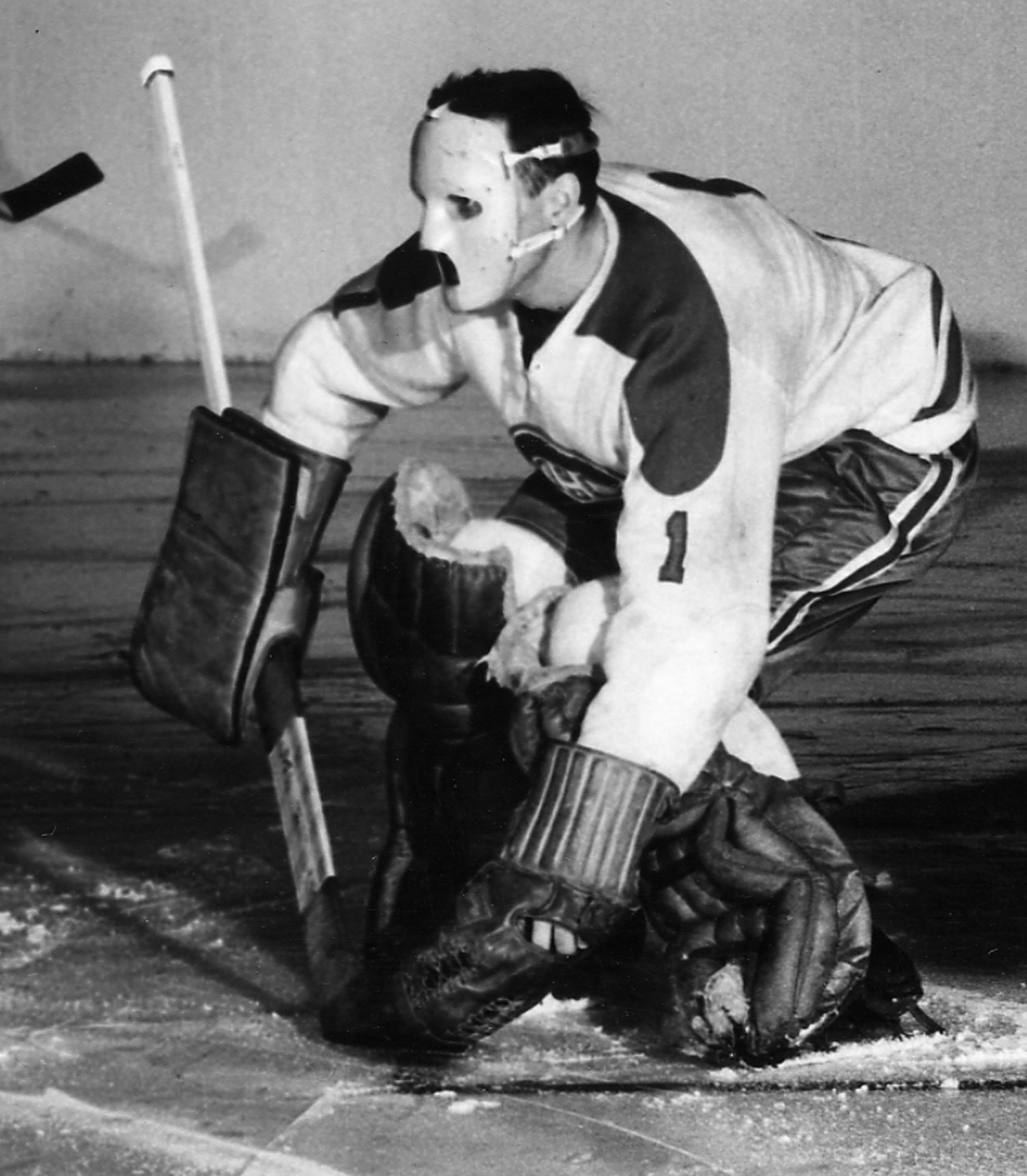 Jacques Plante squatting down in front of the goalie net in 1959 wearing his mask during a game against the Toronto Maple Leafs at Madison Square Garden.