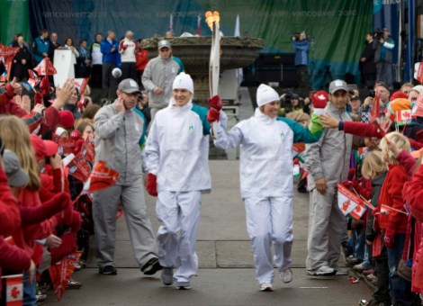 Catrina Le May Doan Simon Whitfield Two torchbearers run through a crowd holding the torch aloft