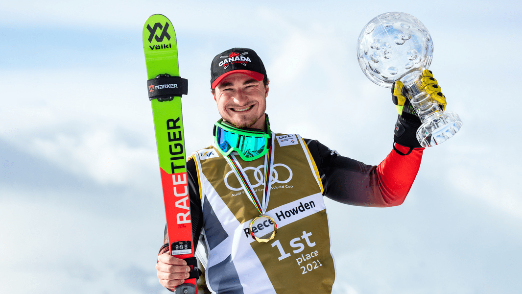 Reece Howden holds up his Crystal Globe in his left hand and his skis in the other.