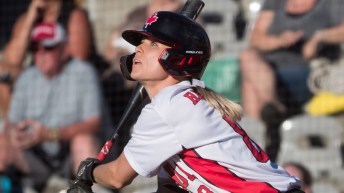 A softball player watches the ball after hitting it with the bat. An out of focus crowd behind her.