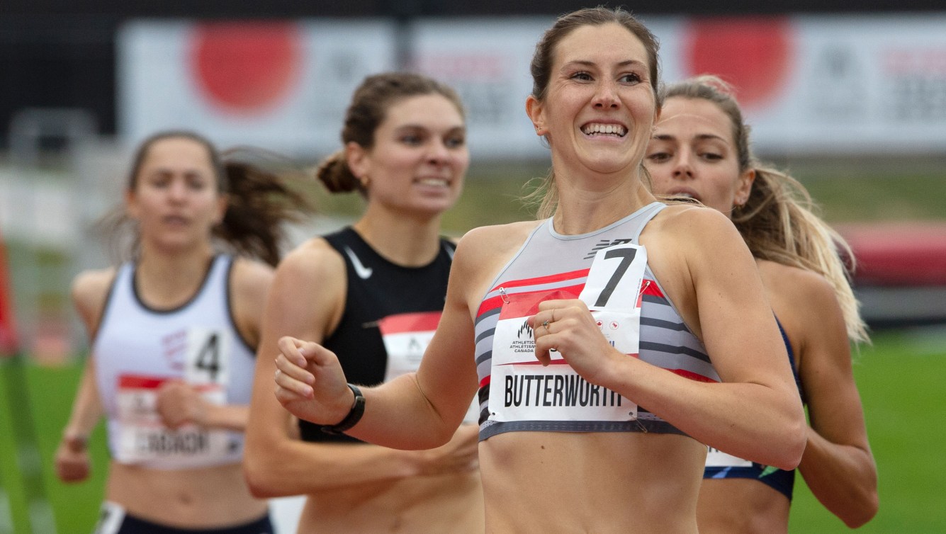 A midshot of Lindsay Butterworth (front) smiling as she wins the 800m race. Behind her are three other runners.