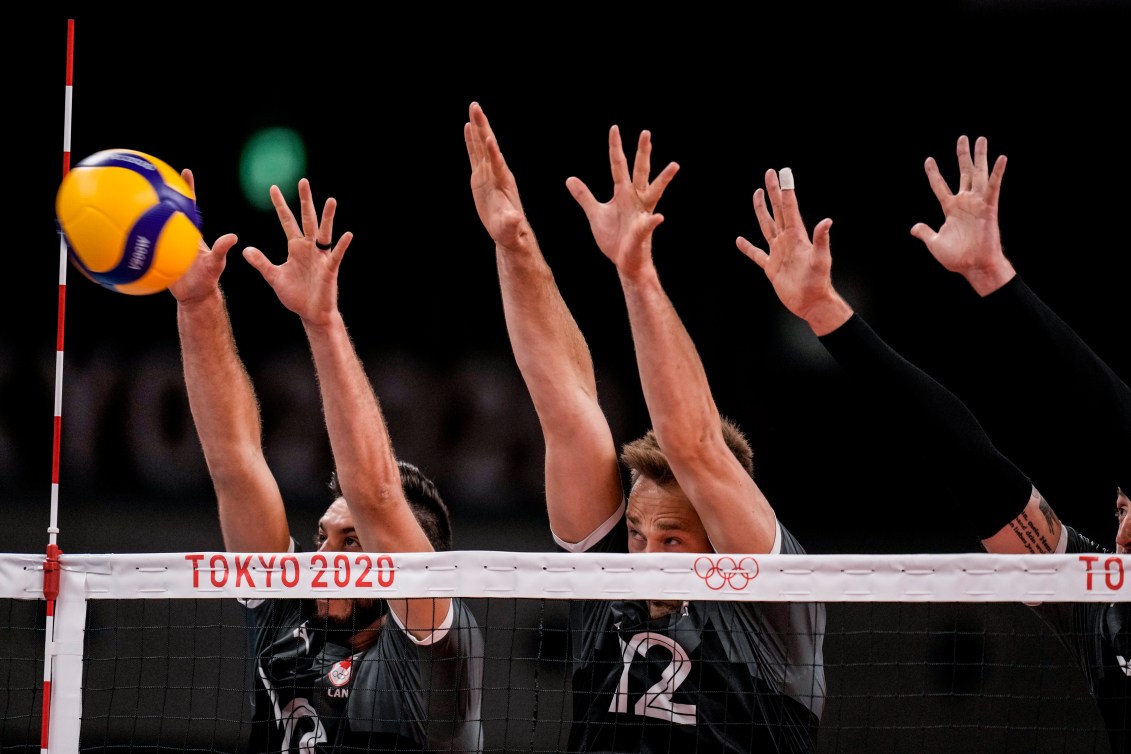 Three Canadian players jump to block the ball at the net